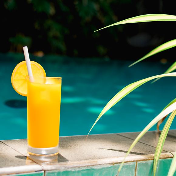 A tall glass of orange juice on the edge of the pool at Amber Poolside.