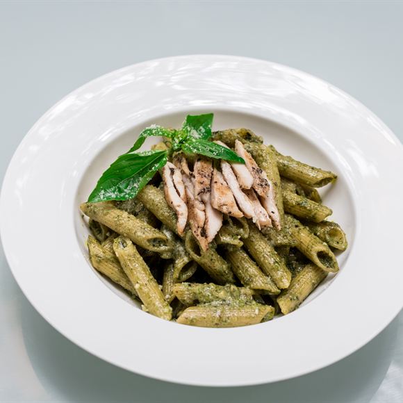 Penne in pesto with chicken, served in a shallow white bowl.