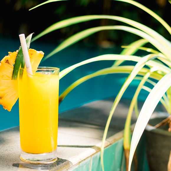 A tall glass of pineapple juice on the edge of the pool at Amber Poolside.