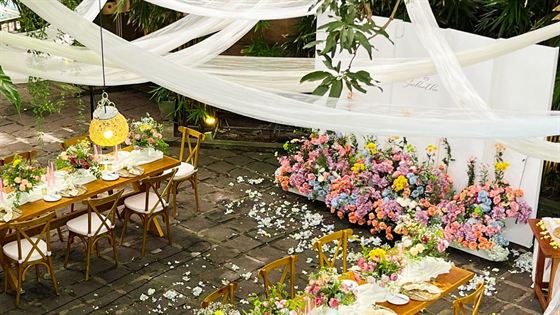 A wedding reception at Amber Poolside, white drapes overhead, long tables under the trees and a bank of pink and cream flowers.