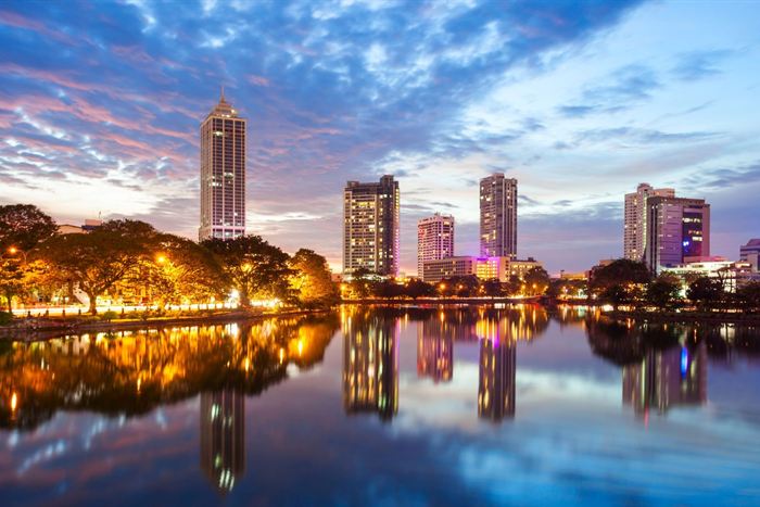 Colombo&rsquo;s towers reflected in still water at dusk, the sky streaked pink and blue.