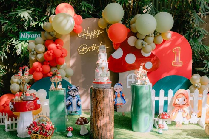 A first birthday set up at Amber Poolside, balloons and a red and green toadstool display among the greenery.