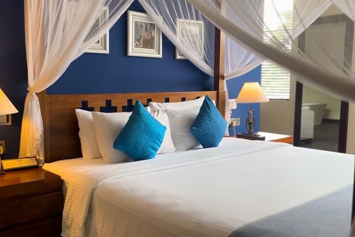 A Luxury Junior Suite at Colombo Court, a four-poster bed with white drapes against a deep blue wall.
