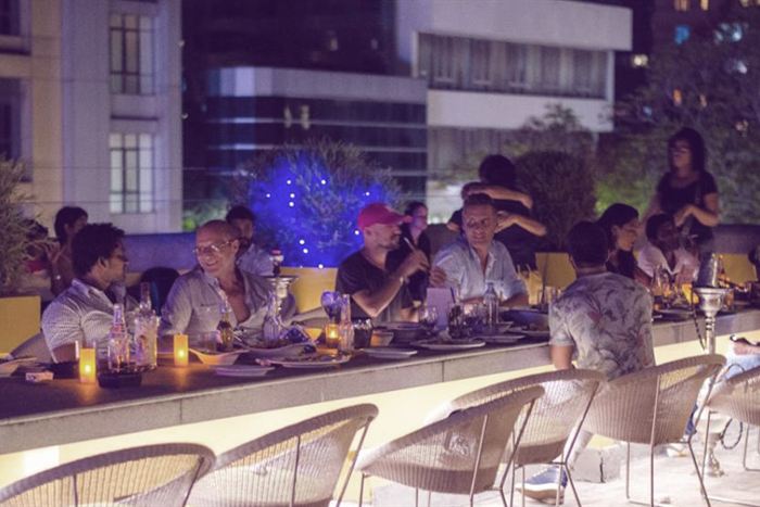 Guests at long tables on the rooftop at Cloud Café & Bar at night, the city lit behind them.