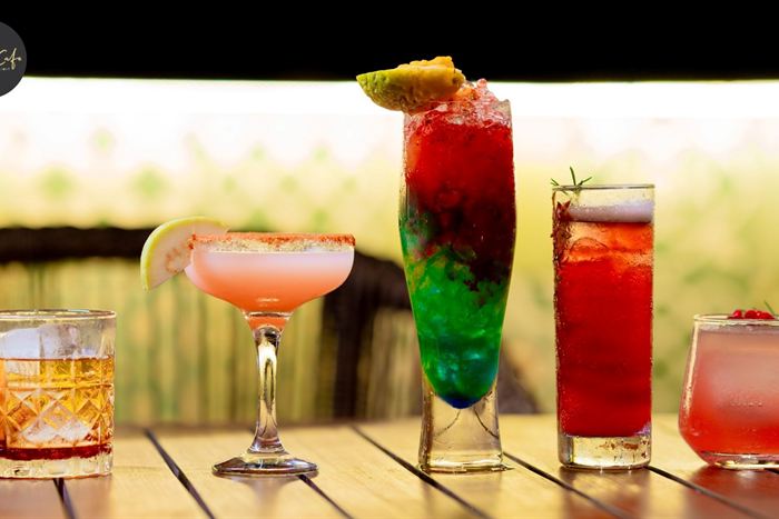 Four cocktails in a row on a timber bar at Cloud Caf&eacute; & Bar, pink, green and amber against a bright backdrop.