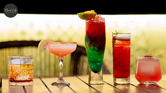 Four cocktails in a row on a timber bar at Cloud Caf&eacute; & Bar, pink, green and amber against a bright backdrop.