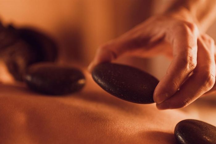 A therapist’s hands placing dark heated stones on a guest’s back during a hot stone massage.