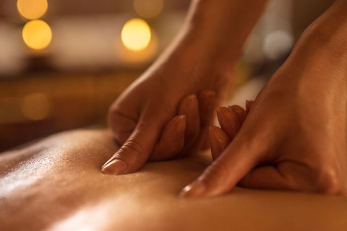 A therapist&rsquo;s hands pressing along a guest&rsquo;s back during a massage, warm light behind.