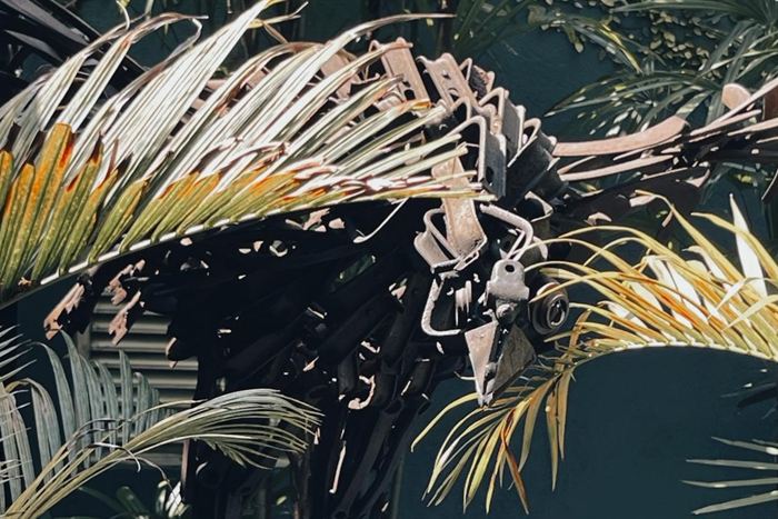Palm fronds sculpted from scrap metal against a dark wall at Colombo Court, real palms in front.