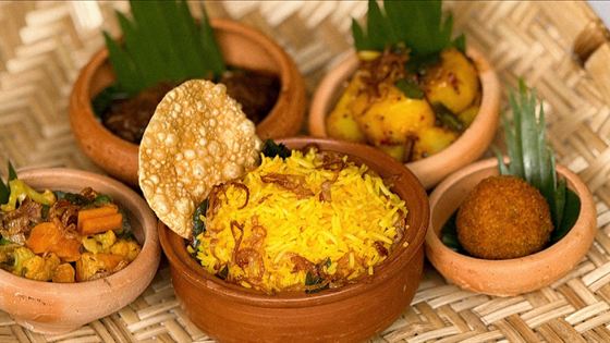 Sri Lankan rice and curries served in clay pots on a woven mat, yellow rice, pappadam and vegetable curries.