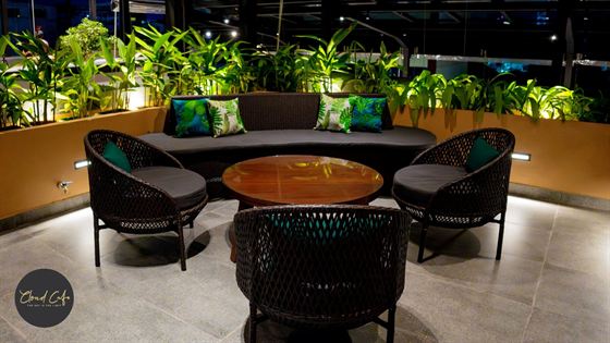 Low sofas and cane chairs around a timber table on the rooftop at Cloud Caf&eacute; & Bar at night, planted beds behind.