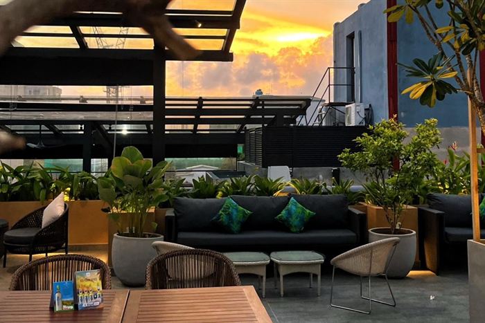 The rooftop at Cloud Caf&eacute; & Bar at sunset, sofas and planters under an orange sky.