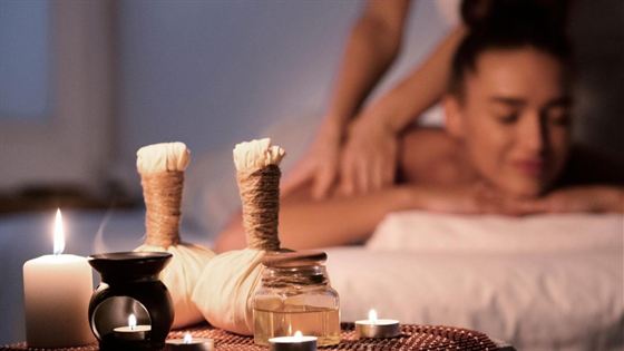 A woman lying face down on a treatment bed at the spa, herbal compresses and a candle beside her.