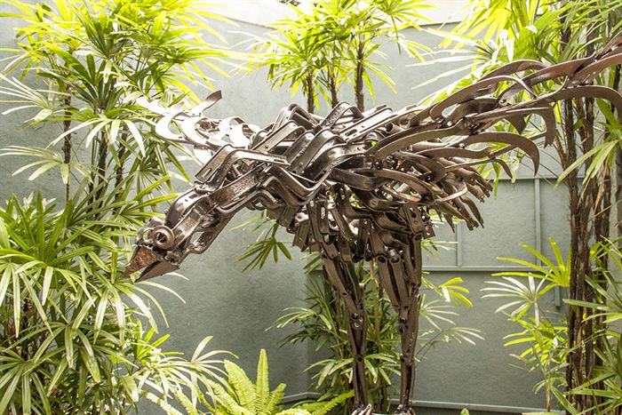A large bird sculpted from scrap metal perched among palms in the garden at Colombo Court.