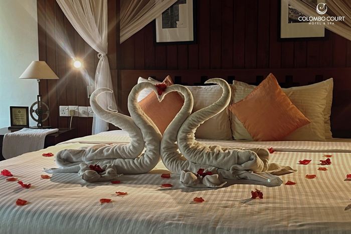 Two swans folded from white towels forming a heart on a bed scattered with rose petals.