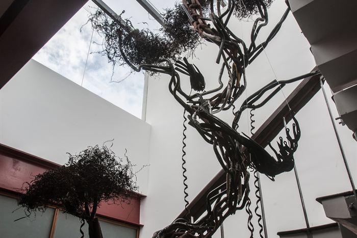 A tree sculpted from scrap steel rising through the building towards a glass roof.