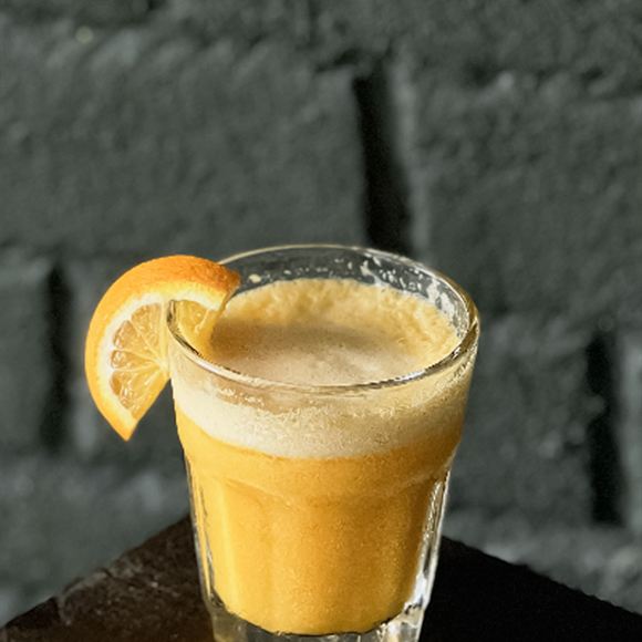 A tall citrus cocktail over ice with an orange slice on the glass.