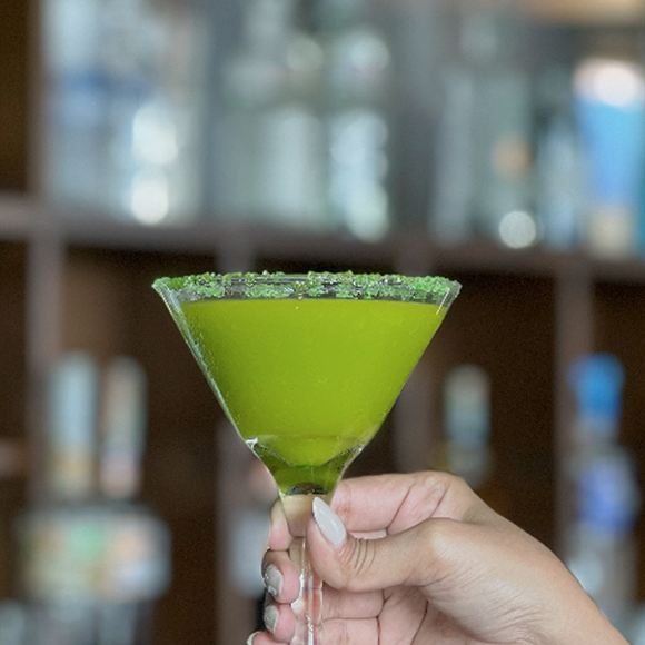 A green cocktail in a salt-rimmed martini glass, held up in front of the bar.
