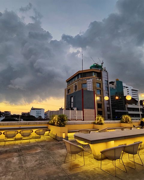 Colombo rooftops at sunset seen from Cloud Caf&eacute; & Bar, lanterns strung against a gold and grey sky.