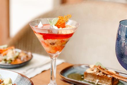 A cocktail in a coupe glass beside small plates at Amber Poolside.