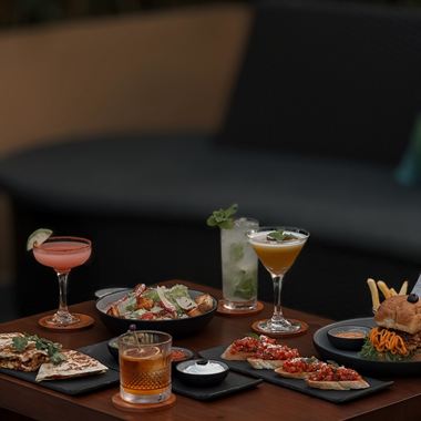 Cocktails and small plates across a dark timber table at Cloud Caf&eacute; & Bar.