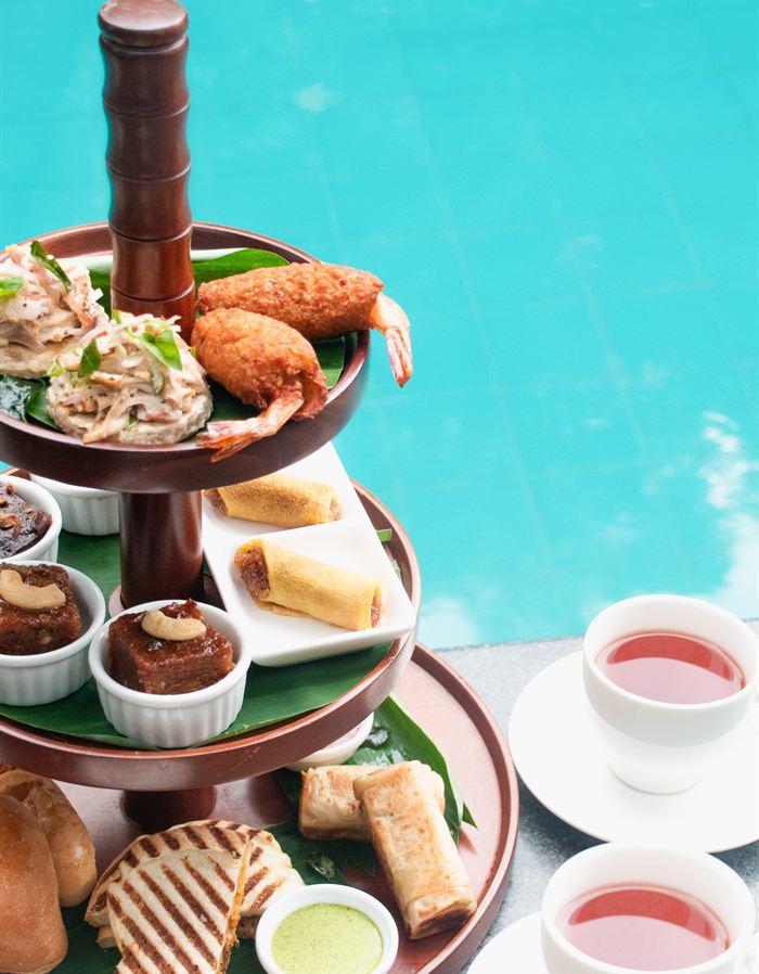 A Ceylon high tea stand at Amber Poolside, savouries and sweets on three tiers beside the turquoise pool.