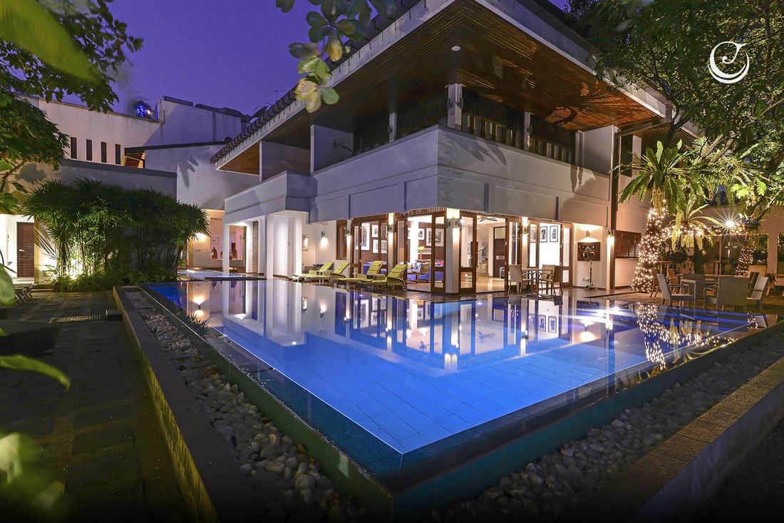 The poolside garden at dusk, the pool lit blue and the hotel glowing around it.
