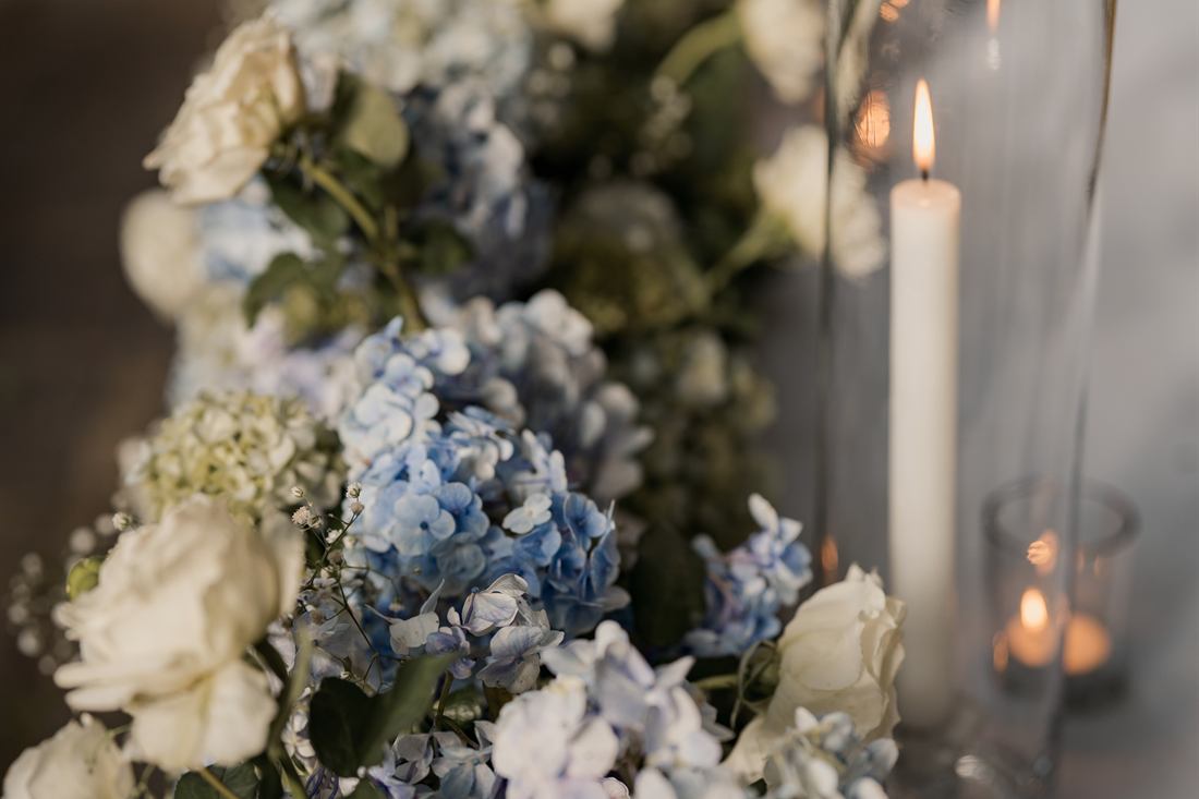 A detail of a wedding table in the poolside garden, white florals and candles in glass.