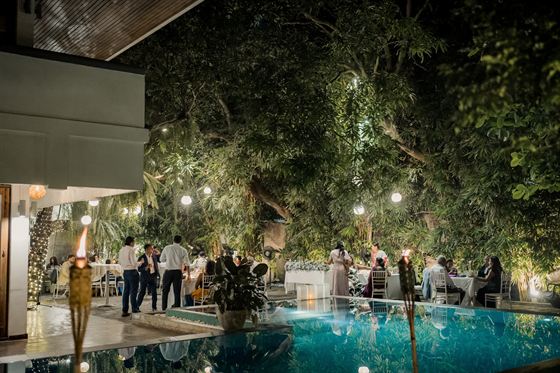 Guests standing with drinks beside the lit pool at Colombo Court after dark.