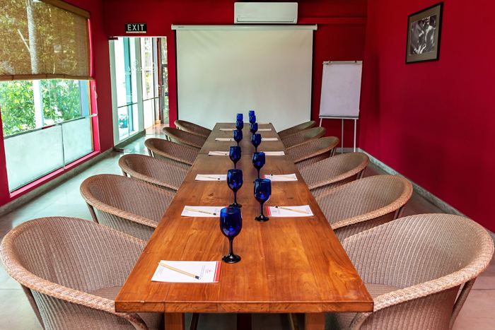 The Scarlet Room set for a meeting, one long timber table under a red wall with a projector screen at the end.