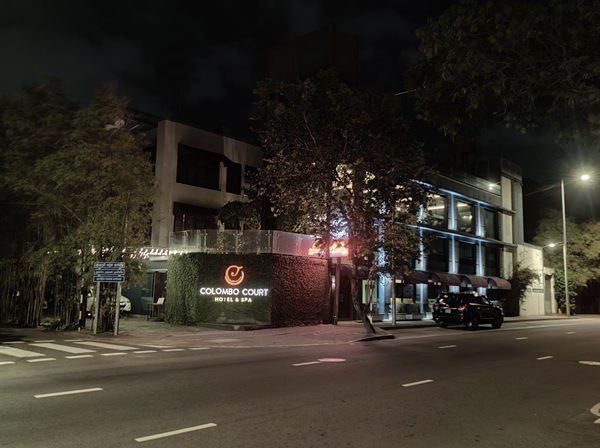 Alfred House Avenue at night outside Colombo Court, the hedge wall lit and traffic passing.