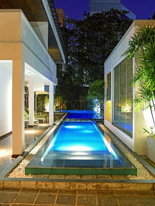 The pool at Colombo Court lit blue at night between the white walls of the garden.