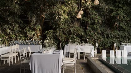 A table set beside the pool under the trees, ready for a private dinner.