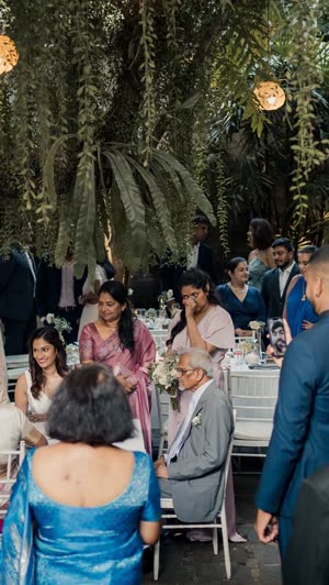 A ceremony in the poolside garden, guests standing between the trees under strings of lights.