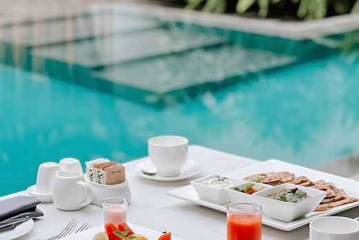 A table of plates and cold drinks at the edge of the turquoise pool at Amber Poolside.