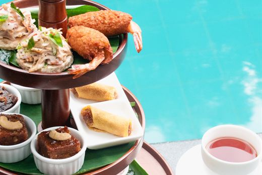 A three-tier high tea stand of savouries and sweets set beside the pool at Amber Poolside.