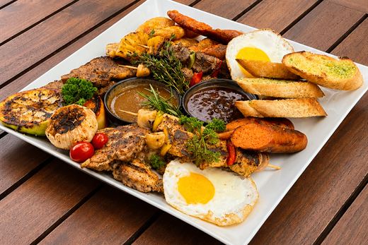 A sharing platter of grilled meats, sausages, eggs and garlic bread on a long white dish.