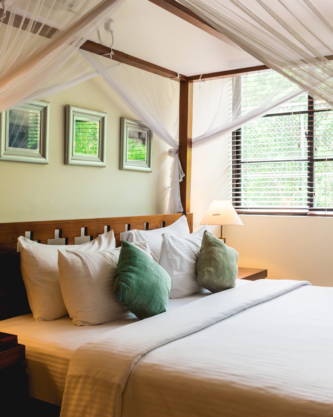The Luxury Duplex Suite, a four-poster bed under a net beside a window full of trees.