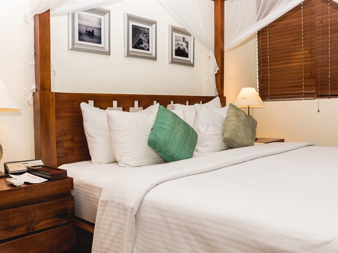 The four-poster bed in the Luxury Duplex Suite against timber blinds.