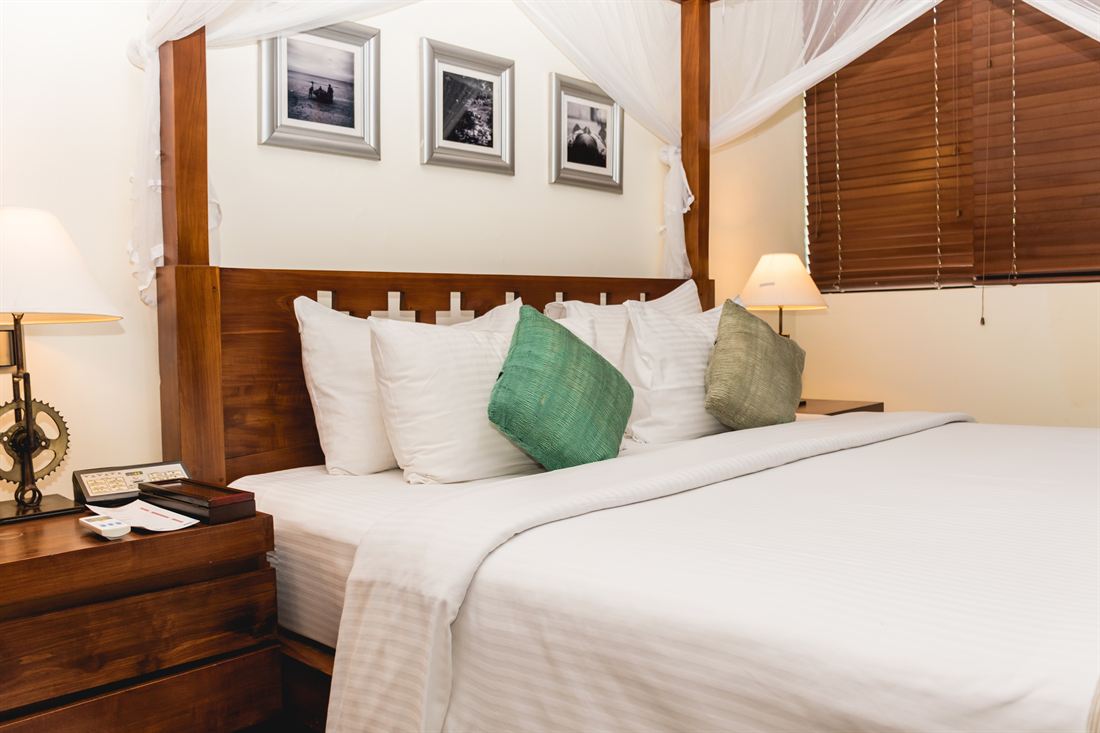 The bed in the Luxury Duplex Suite, green cushions and framed prints above the headboard.
