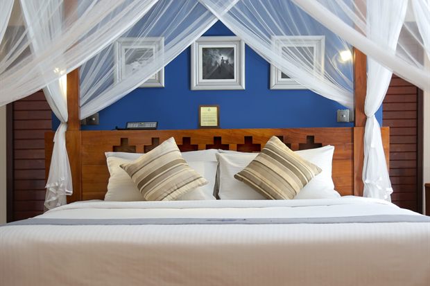The Luxury Honeymoon Suite at Colombo Court, a four-poster bed under a white mosquito net against a deep blue wall.