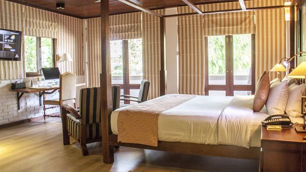 A Luxury Junior Suite at Colombo Court, a timber four-poster bed under a ceiling fan with slatted screens behind it.