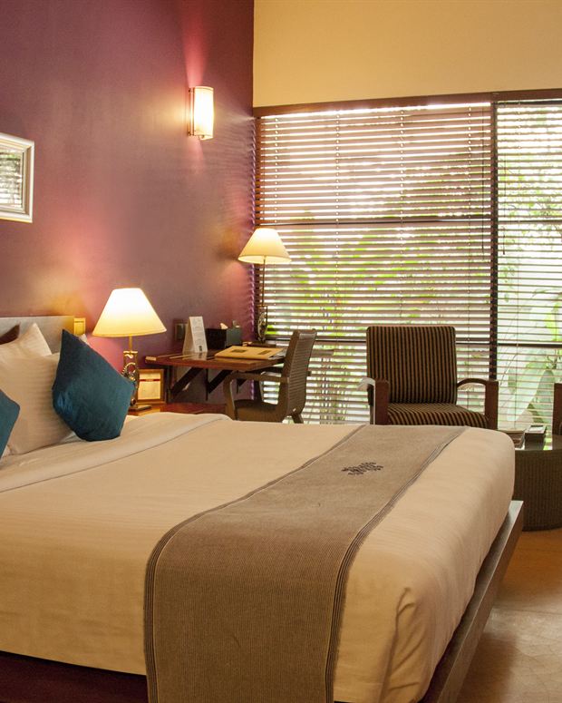A Superior Deluxe room at Colombo Court, a king bed against a deep red wall with a window onto the garden.