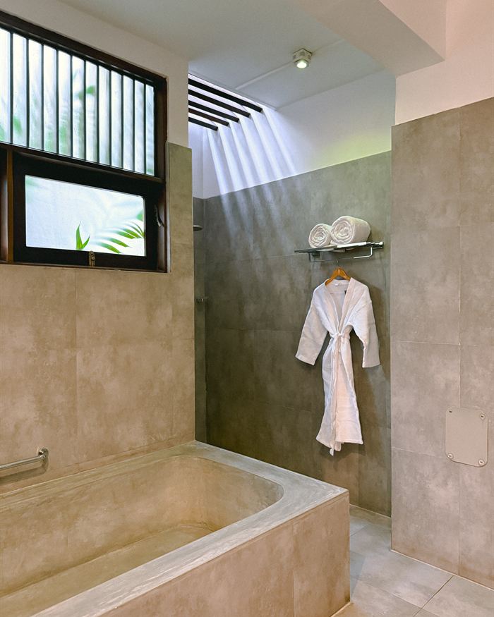 A quiet treatment room at The Court Spa, a white robe hanging beside a stone bath in soft daylight.