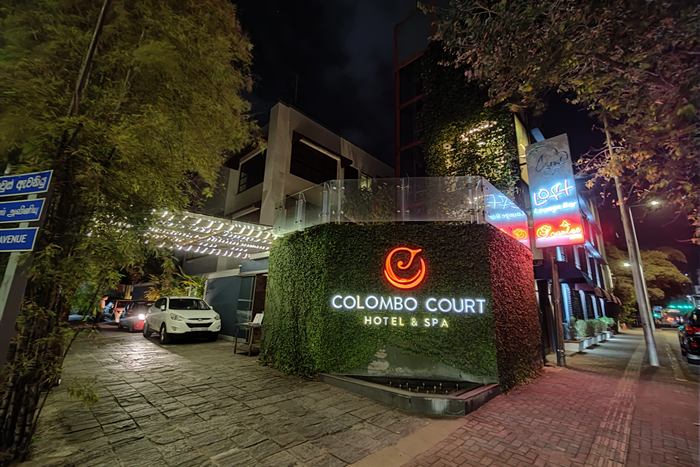 The entrance to Colombo Court Hotel and Spa at night, the sign lit on a wall of green planting.