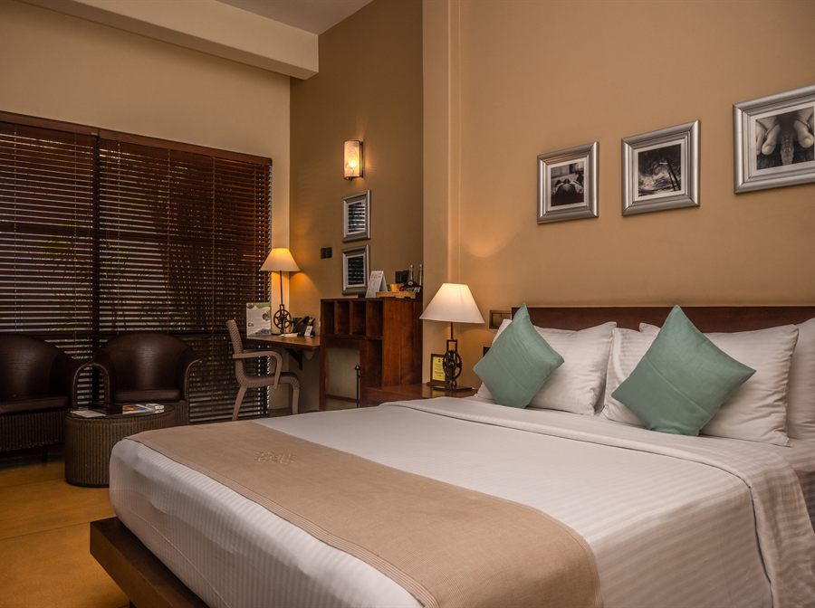 A Deluxe room at Colombo Court with a queen bed, a writing desk and a leather armchair.