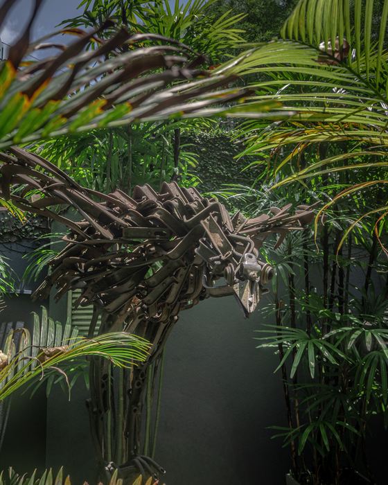 A bird sculpted from pieces of scrap metal among palms in the garden at Colombo Court.