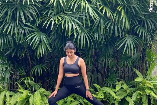 A guest holding a standing yoga pose against a wall of palms and ferns at Colombo Court.