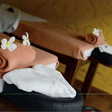 Rolled towels and frangipani flowers on a treatment bed.