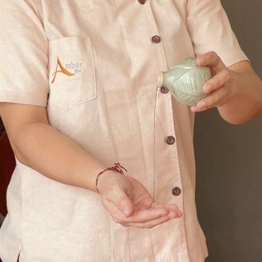 A therapist in a spa uniform warming massage oil in the palm of one hand.